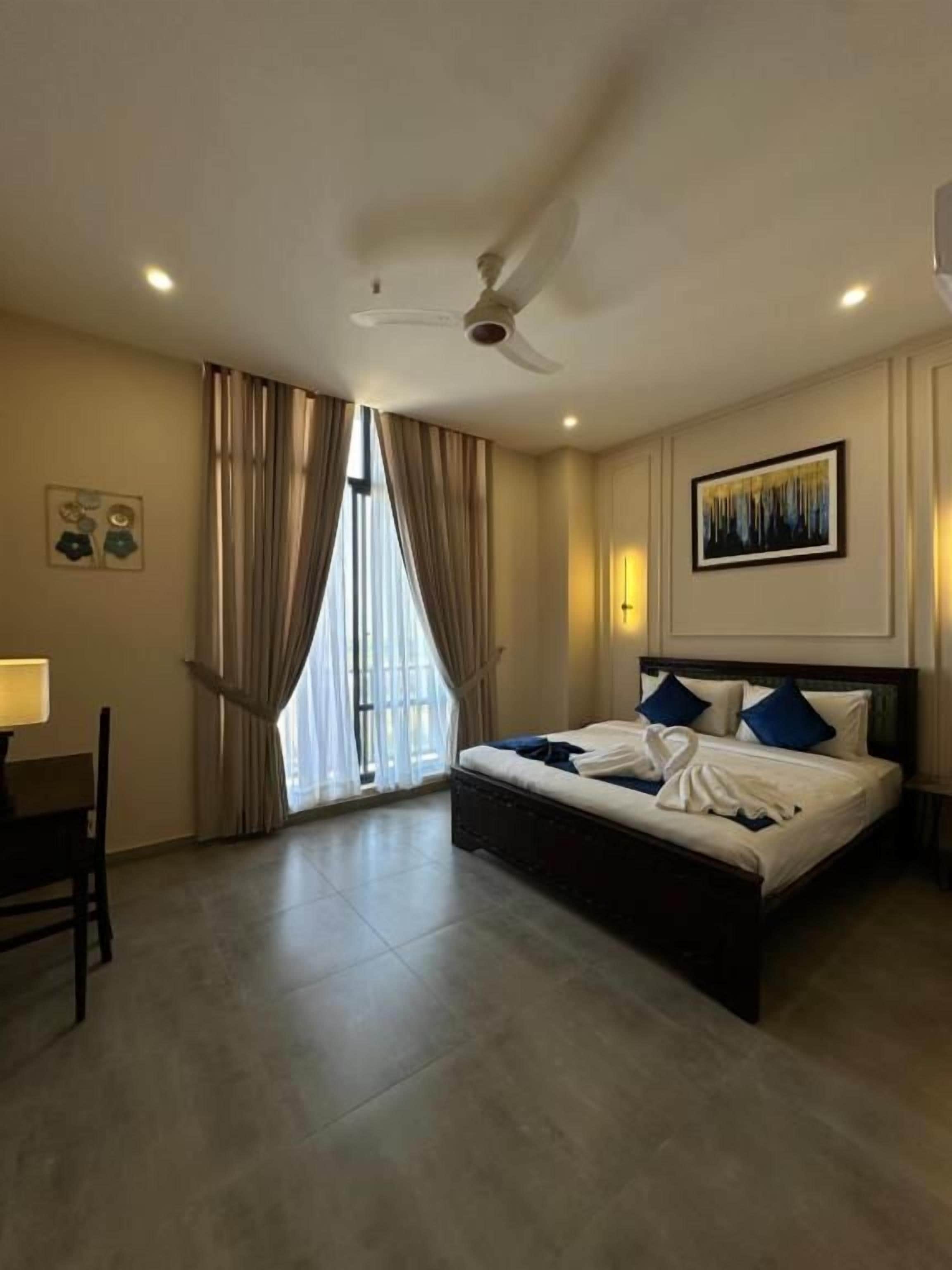 A hotel room with a bed, a desk, a chair, a ceiling fan, and a window with curtains.