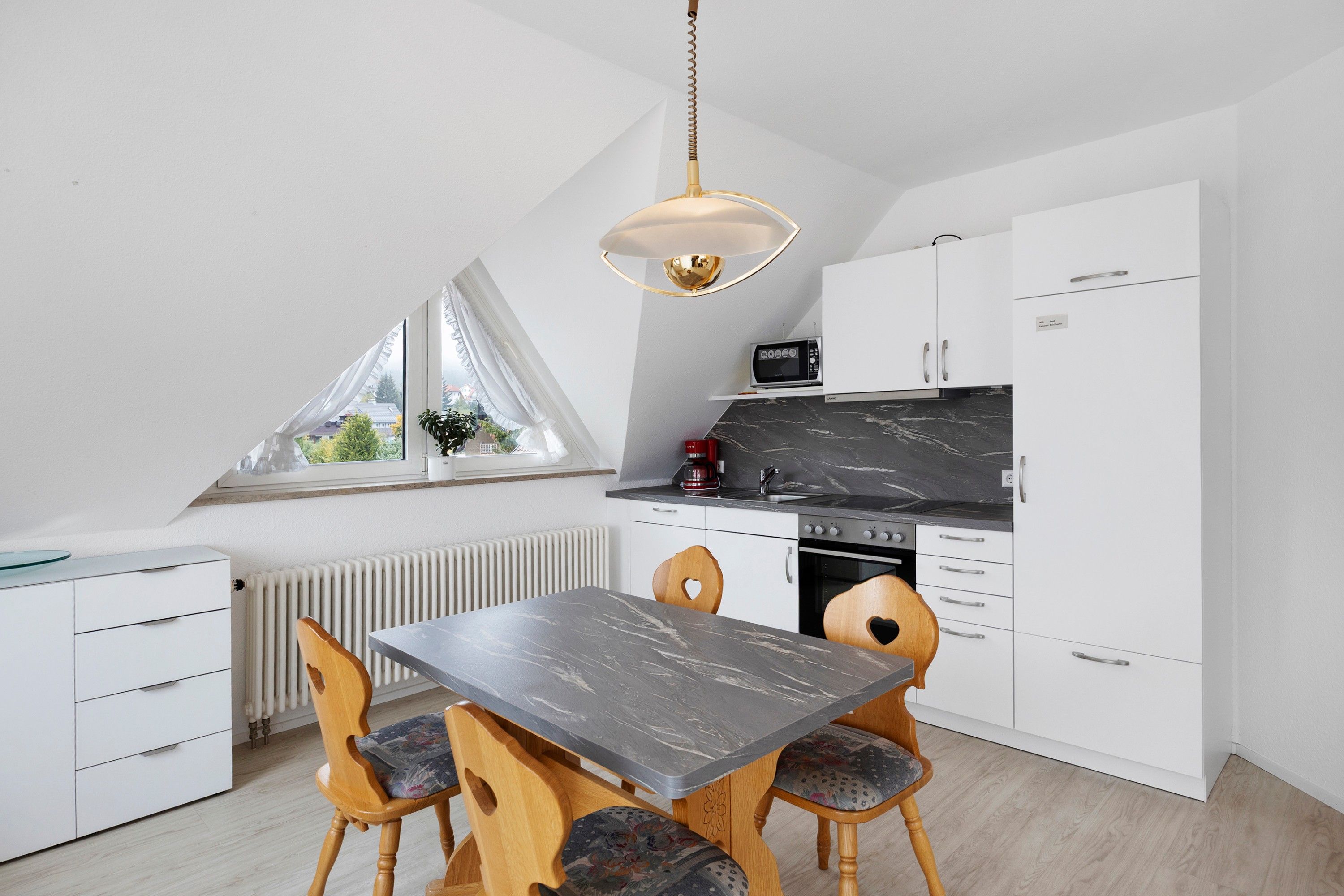 Eine moderne Küche mit Esstisch und Stühlen, einem Fenster mit Vorhängen sowie einer Deckenleuchte.