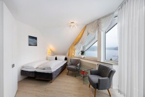 Ein modernes Schlafzimmer mit Bett, Sessel, Glastisch und Blick auf das Wasser.