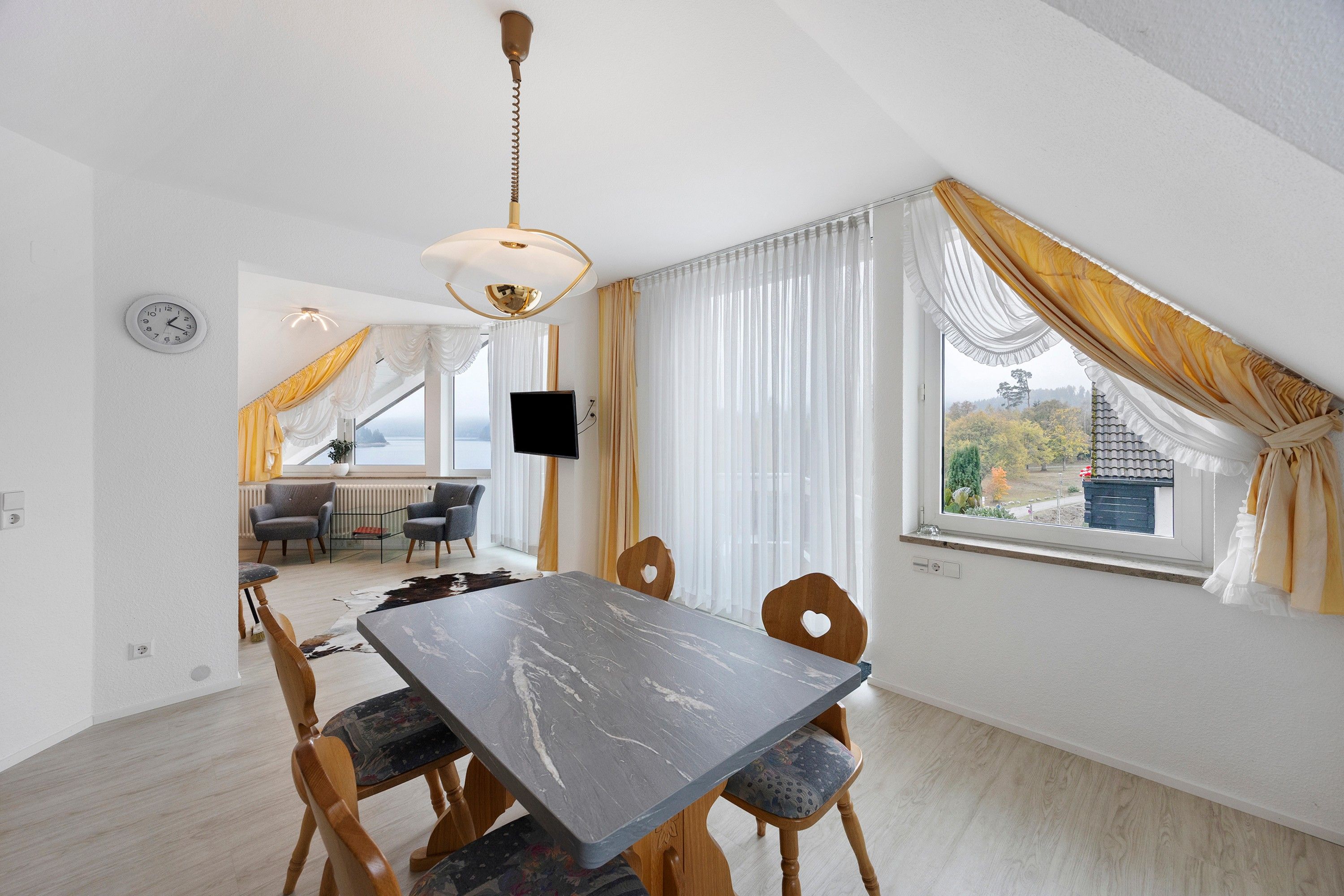 Ein Essbereich mit Tisch und Stühlen, einem Fernseher und Blick ins Freie.