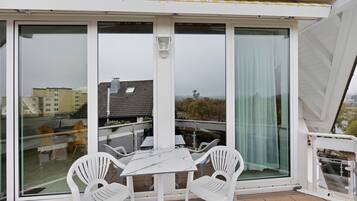 Ein Balkon mit Tisch und Stühlen, großen Fenstern und Blick auf Gebäude und Bäume.