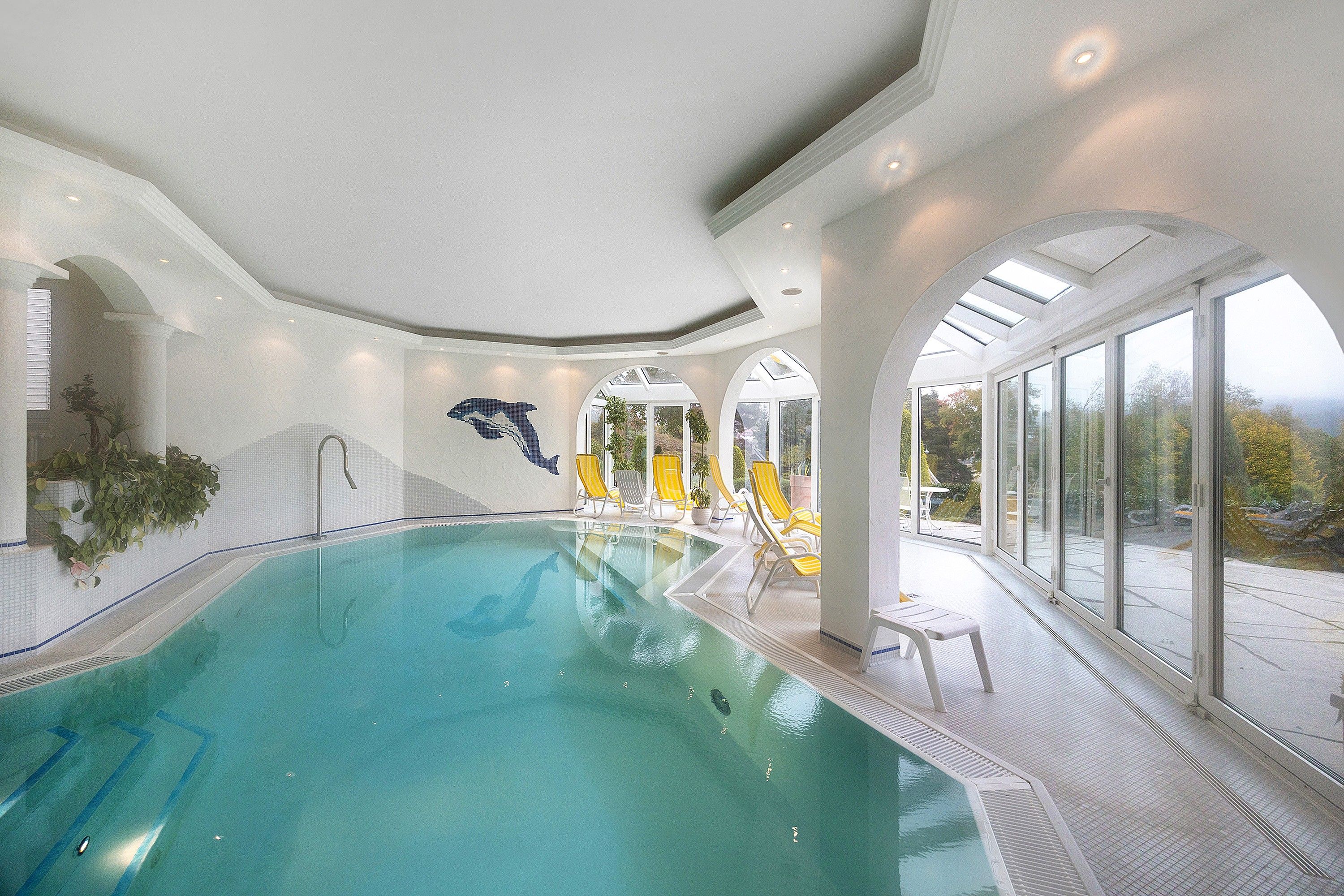 Ein überdachter Pool mit Panoramafenstern, gelben Liegestühlen und Wandmalerei mit Delphinen.