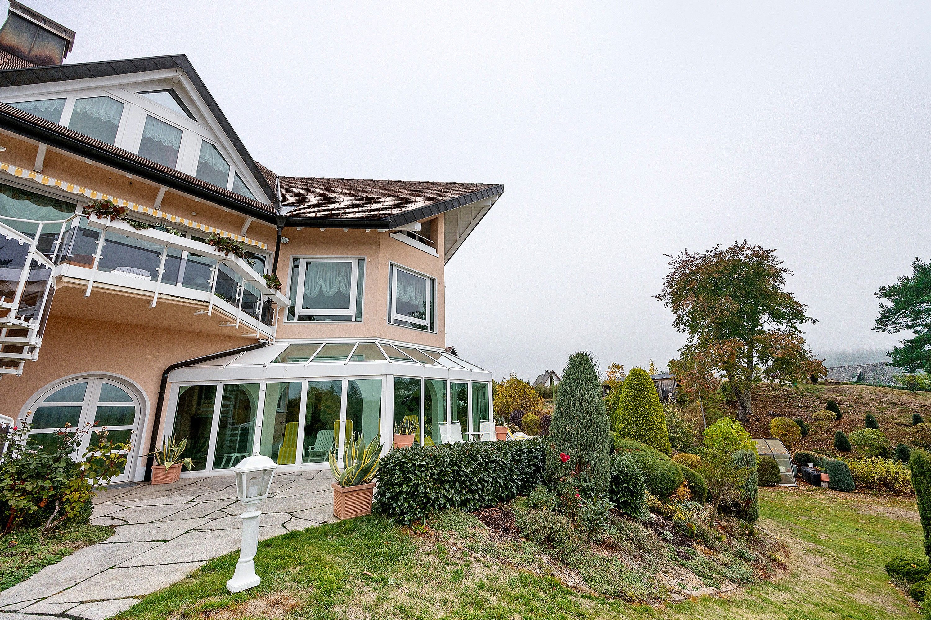 Ein zweistöckiges Haus mit Wintergarten, Balkon und gepflegtem Garten.