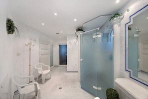 Une salle de bain moderne avec une douche à parois de verre, une chaise blanche et un grand miroir.