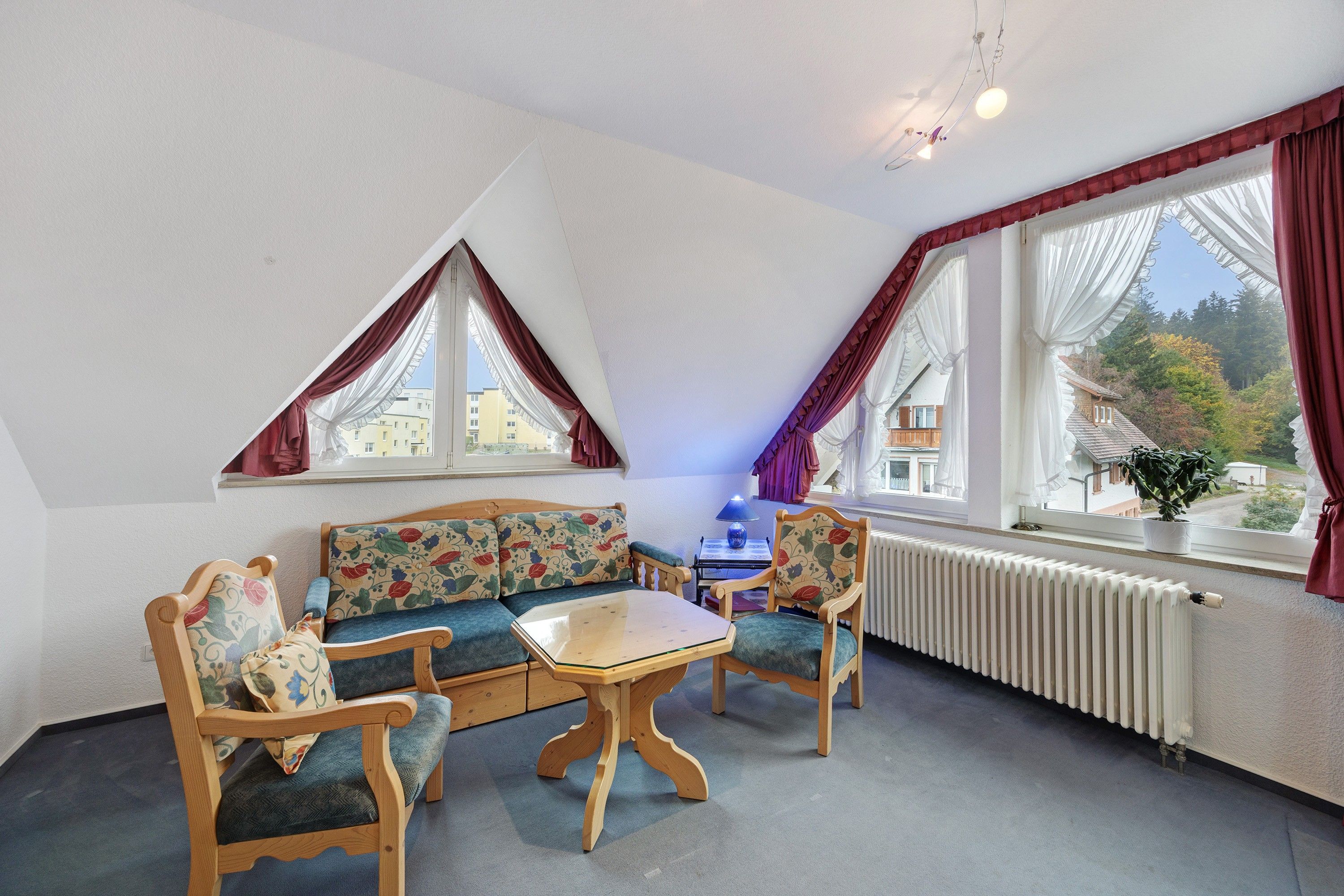 Une pièce chaleureuse avec un canapé en bois, deux fauteuils, une petite table et un radiateur.