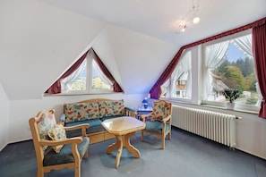 Une pièce chaleureuse avec un canapé en bois, deux fauteuils, une petite table et un radiateur.