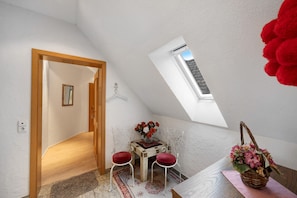 Una habitación con techo inclinado, una pequeña mesa con sillas, un espejo y un ventanal.