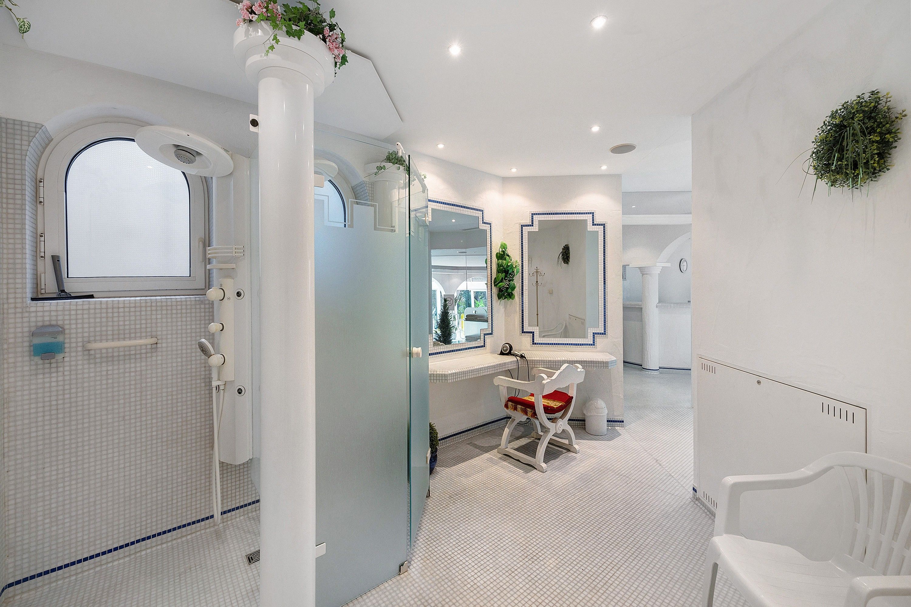 Een moderne badkamer met een douchecabine van glas, een wit wastafelmeubel met spiegel en een witte stoel.