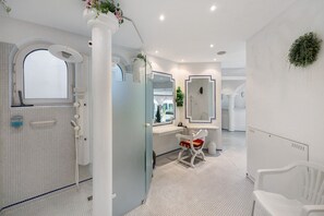 Un baño moderno con cabina de ducha de vidrio, un tocador blanco con espejo y una silla blanca.