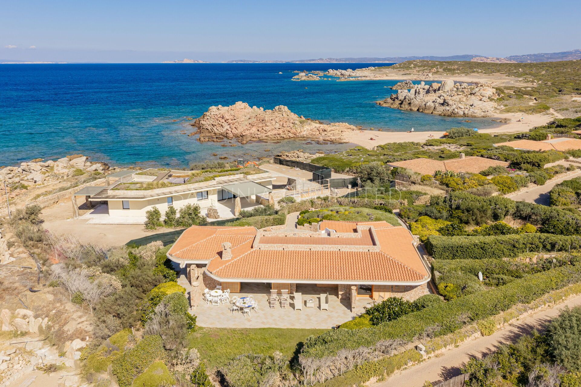 A coastal property with a large house featuring a tiled roof, a patio with outdoor furniture, and a view of the sea.