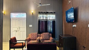 Een kamer met een bank, een stoel, een televisie en een plafondventilator.