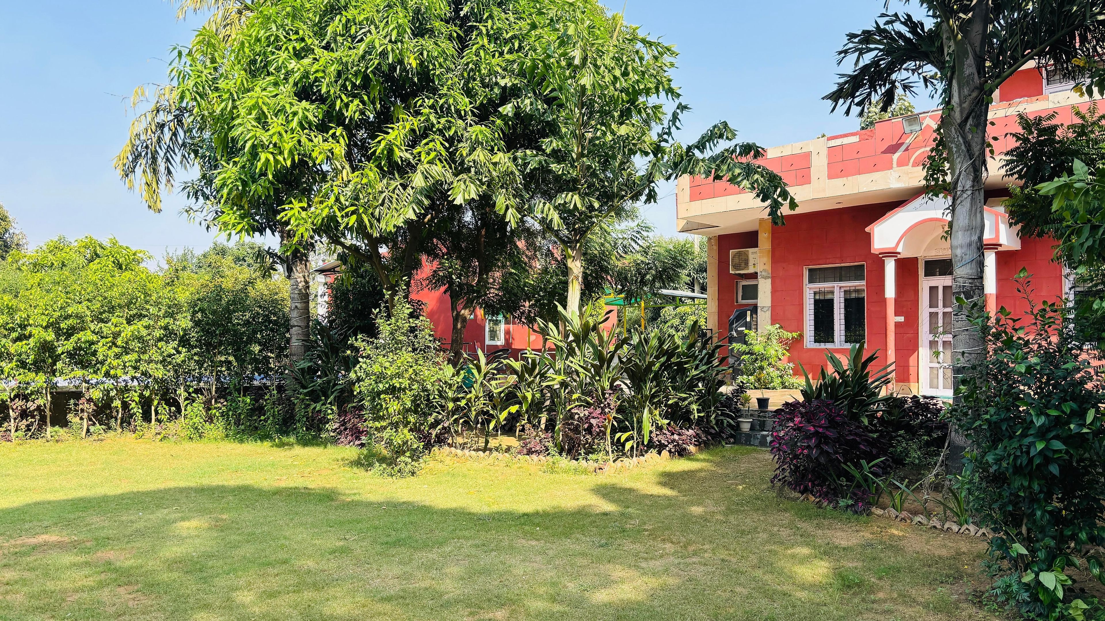 A red building with a garden in front, surrounded by various trees and plants.