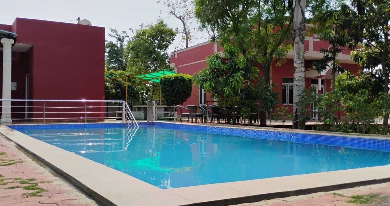 A swimming pool with a tiled edge, surrounded by a paved walkway, and adjacent to a building with a red facade.