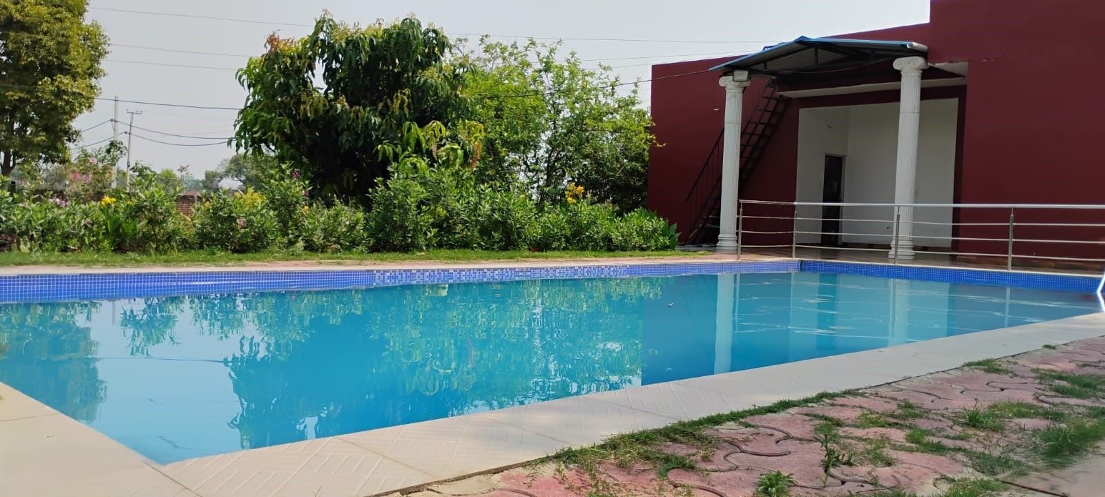 A swimming pool with a tiled edge, surrounded by greenery and a building with a red facade.