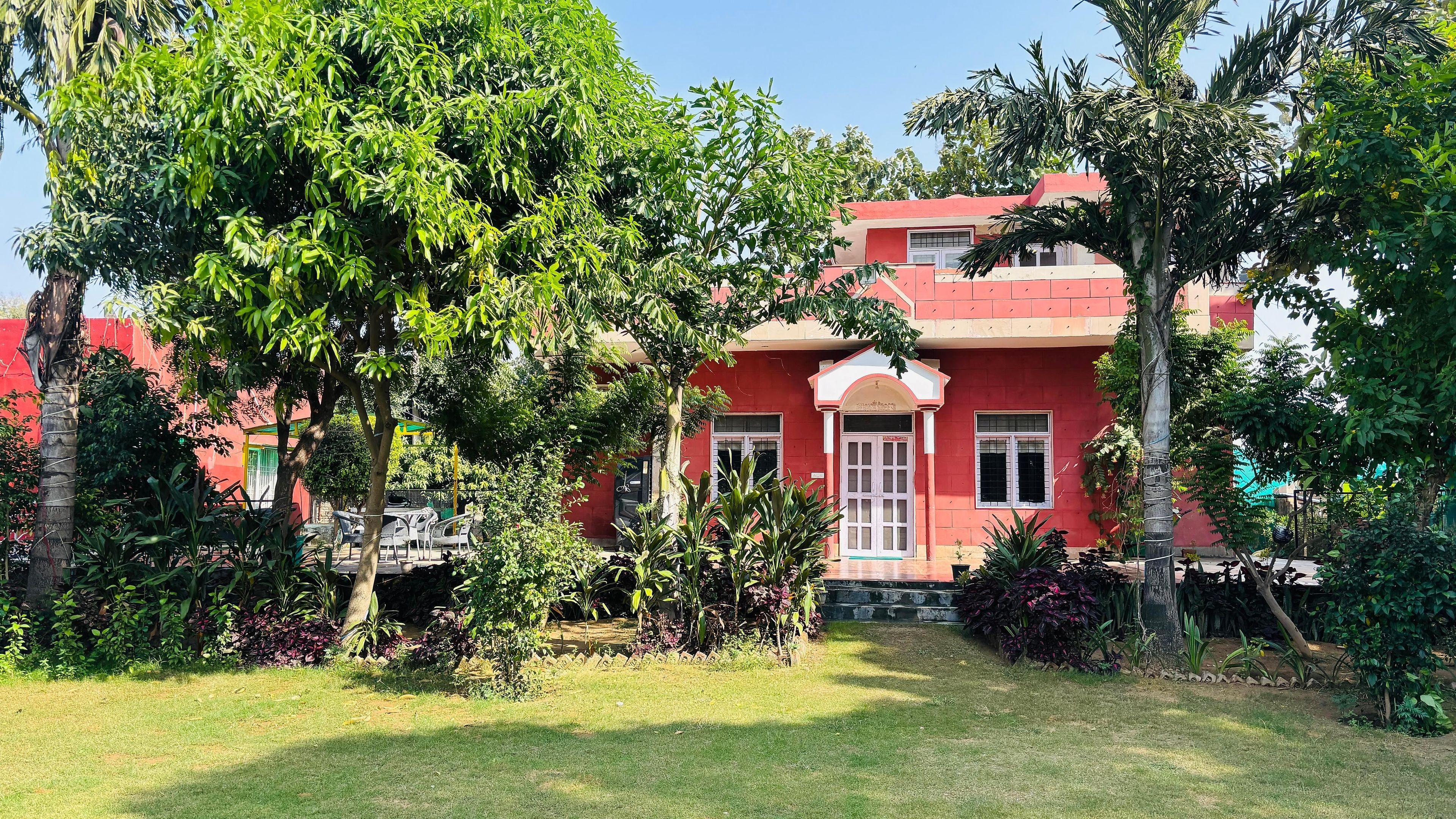 A red building with a central entrance, surrounded by lush greenery and a well-maintained lawn.