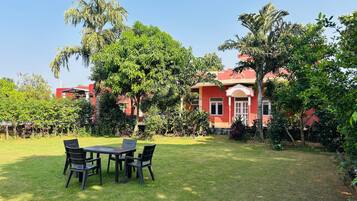 A red building with a garden in front, a table with chairs, and a clear sky.