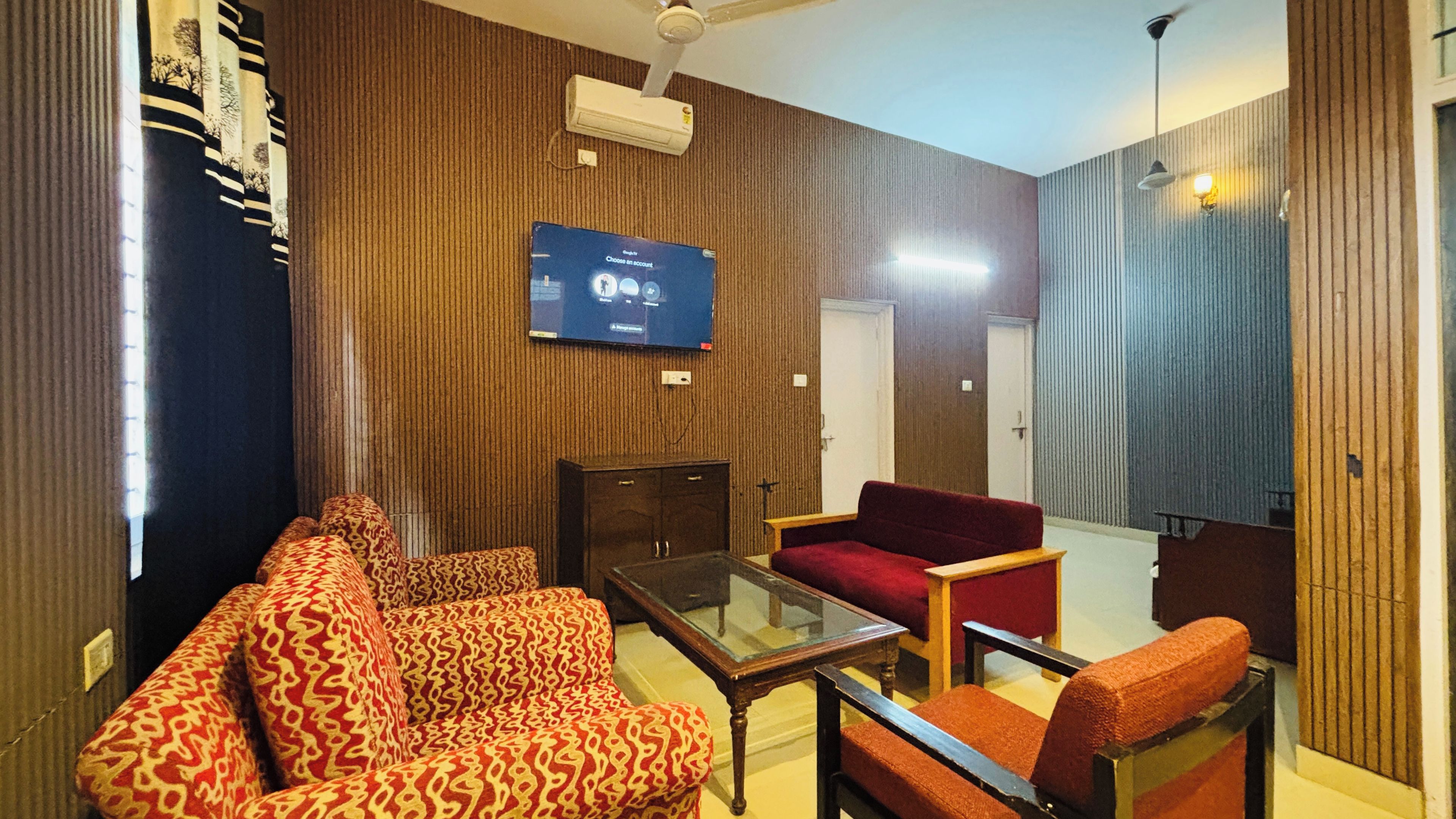 A living room with patterned sofas, a glass coffee table, and a flat-screen TV mounted on the wall.
