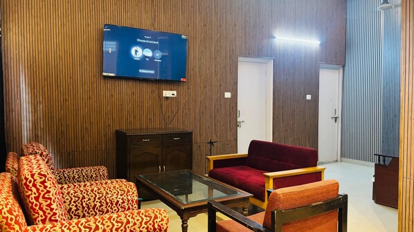 Een hotelkamer met een aan de muur bevestigde televisie, een houten kast, een salontafel met glazen blad en gestreept banken.
