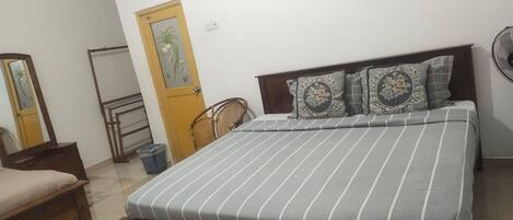 A bedroom with a bed, a wooden headboard, a mirror, a door, and a wall-mounted fan.