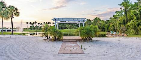 A sandy beach with a pavilion, palm trees, and a body of water.