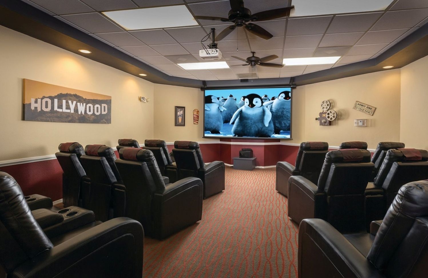 A home theater room with a large screen, multiple reclining chairs, a ceiling fan, and a 'HOLLYWOOD' sign on the wall.