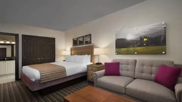 Habitación de hotel con cama, sofá, mesa de centro, escritorio y un cuadro en la pared.