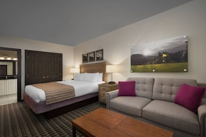 Habitación de hotel con cama, sofá, mesa de centro, escritorio y un cuadro en la pared.