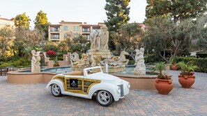 Ein weißer Cabrio parkt vor einem Brunnen mit klassischen Statuen.