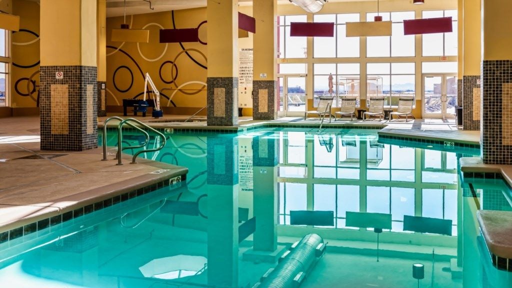 Une piscine intérieure à l’eau claire, entourée de murs recouverts de carreaux et dotée de grandes fenêtres.