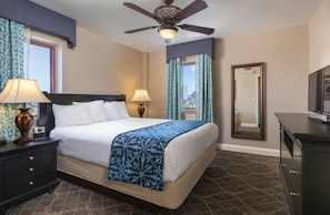 Una habitación de hotel con una cama, dos lámparas de noche, un ventilador de techo, un aparador y un espejo.