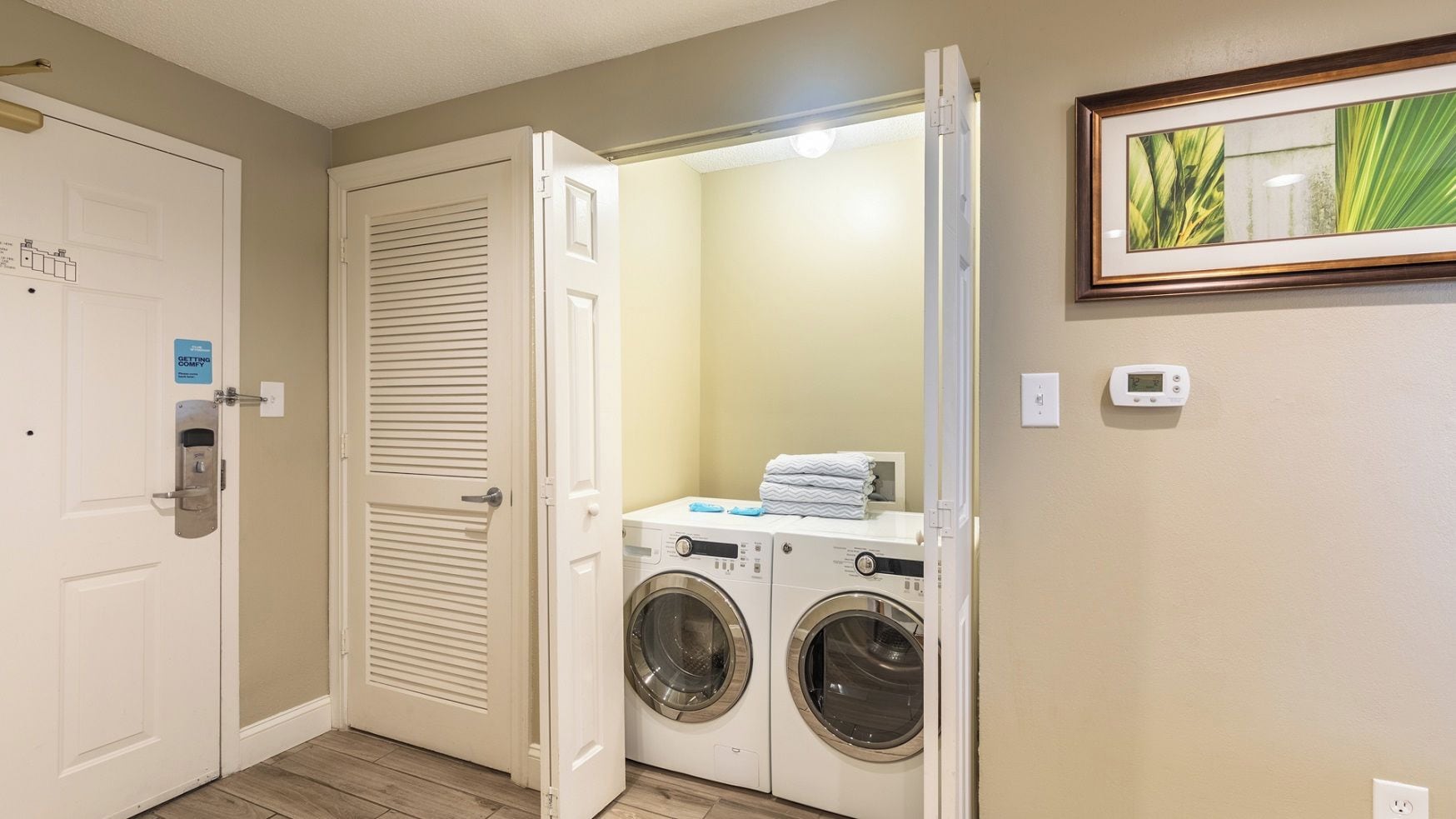 A laundry room with a washing machine and dryer, a door with a lock, and a thermostat on the wall.
