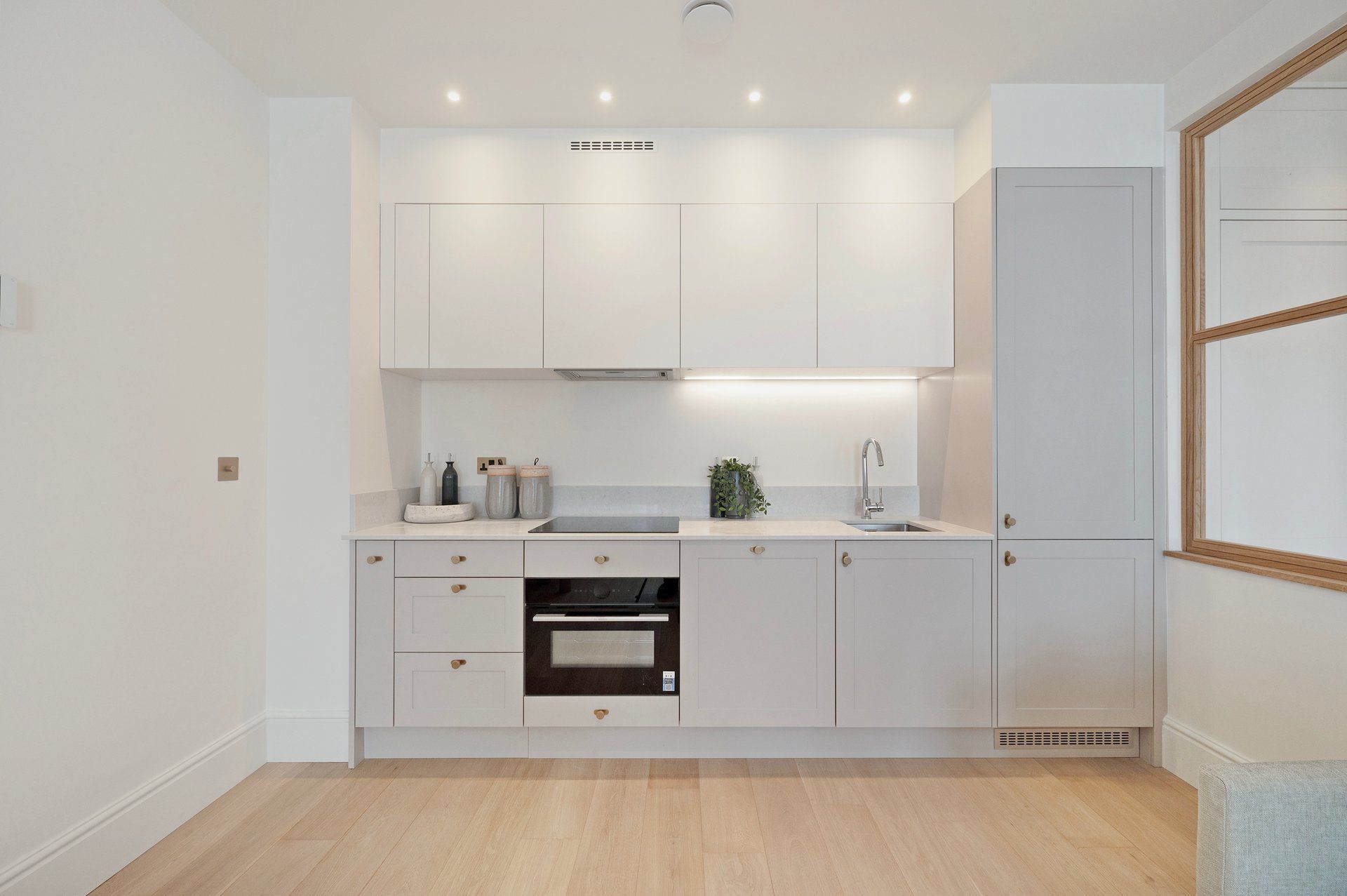 A modern kitchen with white cabinetry, a built-in oven, and a countertop with a sink and decorative items.