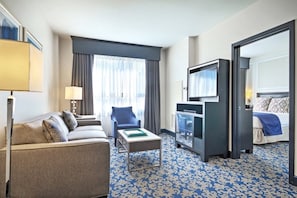 Quarto de hotel com sofá, mesa pequena, televisão e cama.