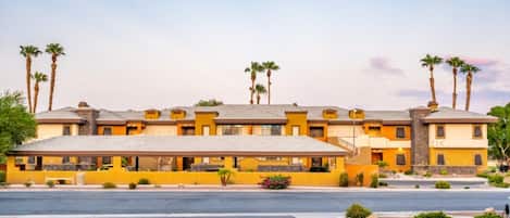 A hotel with a yellow facade, multiple floors, and palm trees.