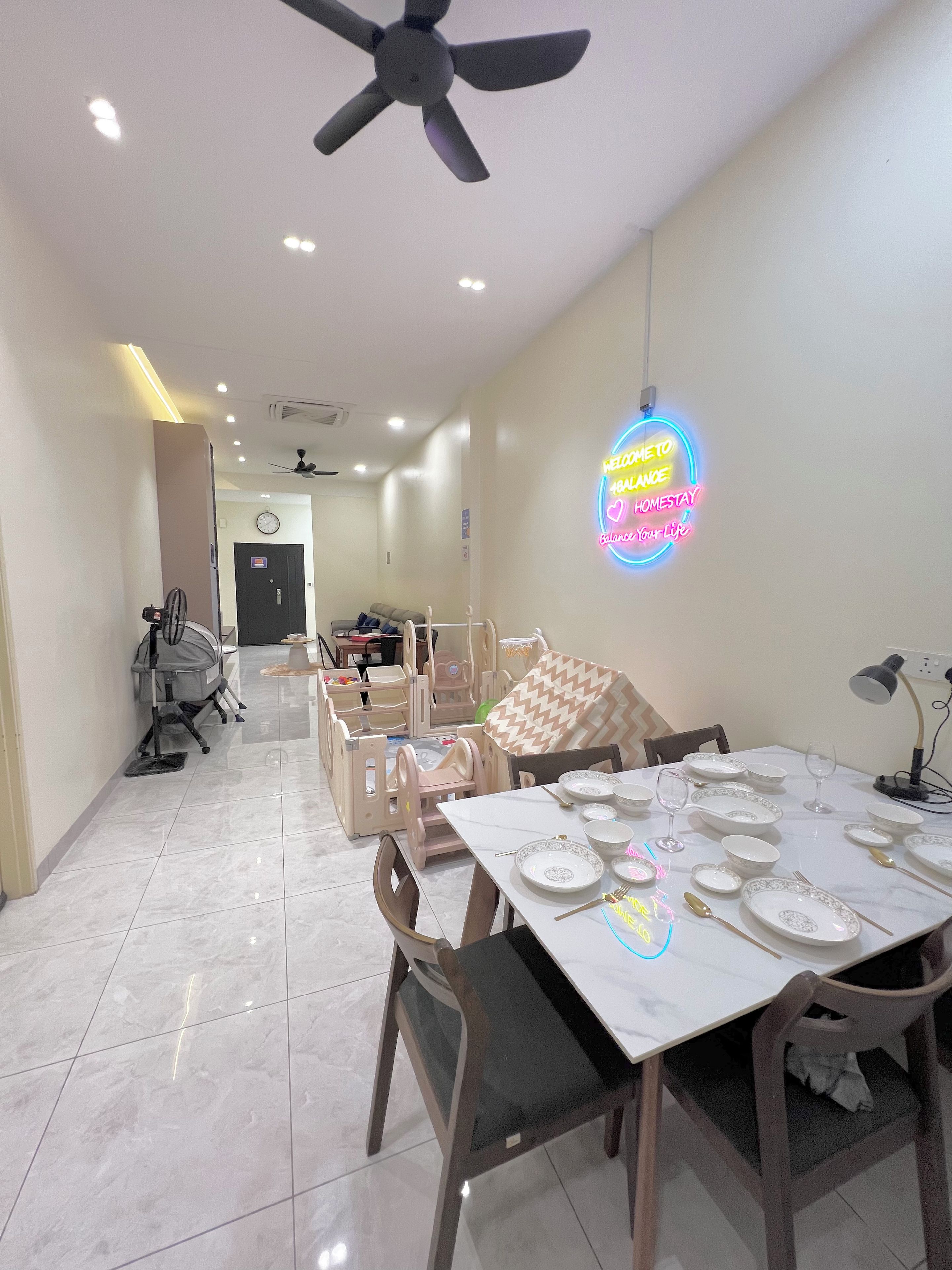 A dining area with a table set for four, chairs, a ceiling fan, and a neon sign on the wall.