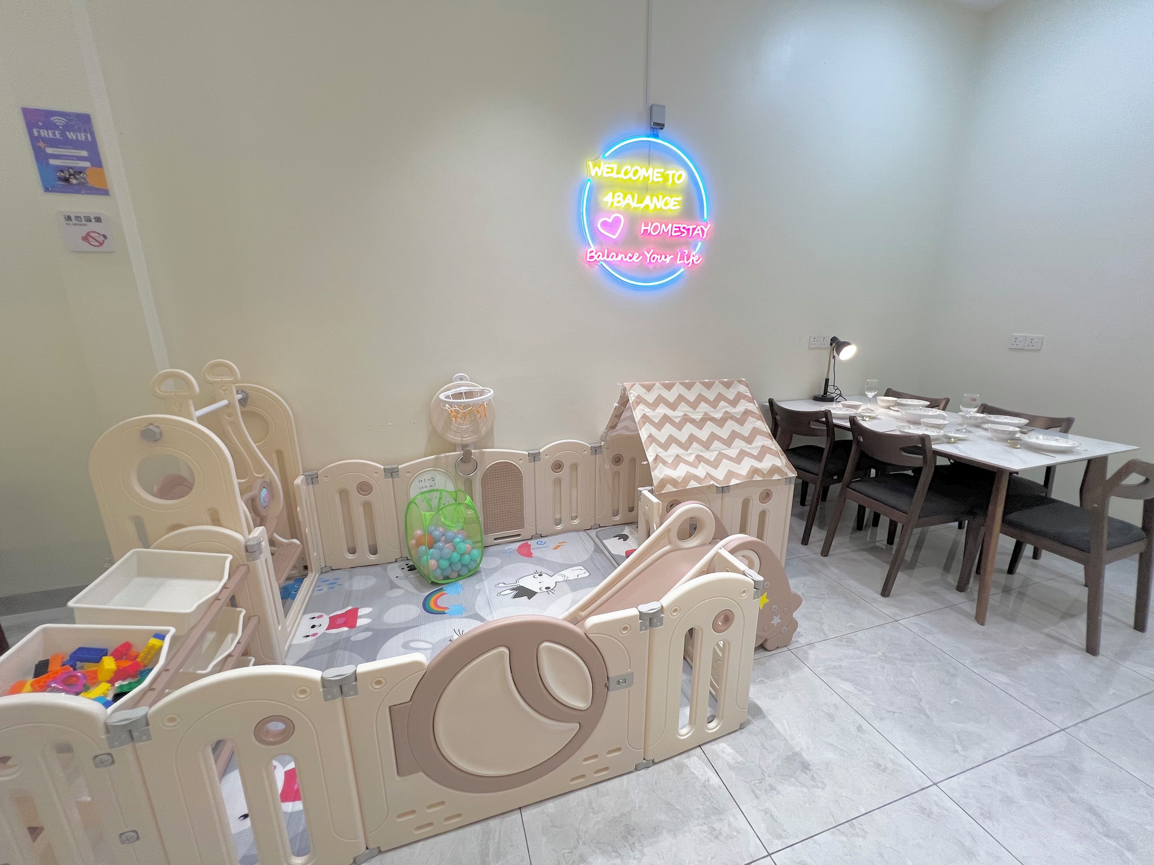 A children's play area with a soft play structure, a table with chairs, and a neon sign.