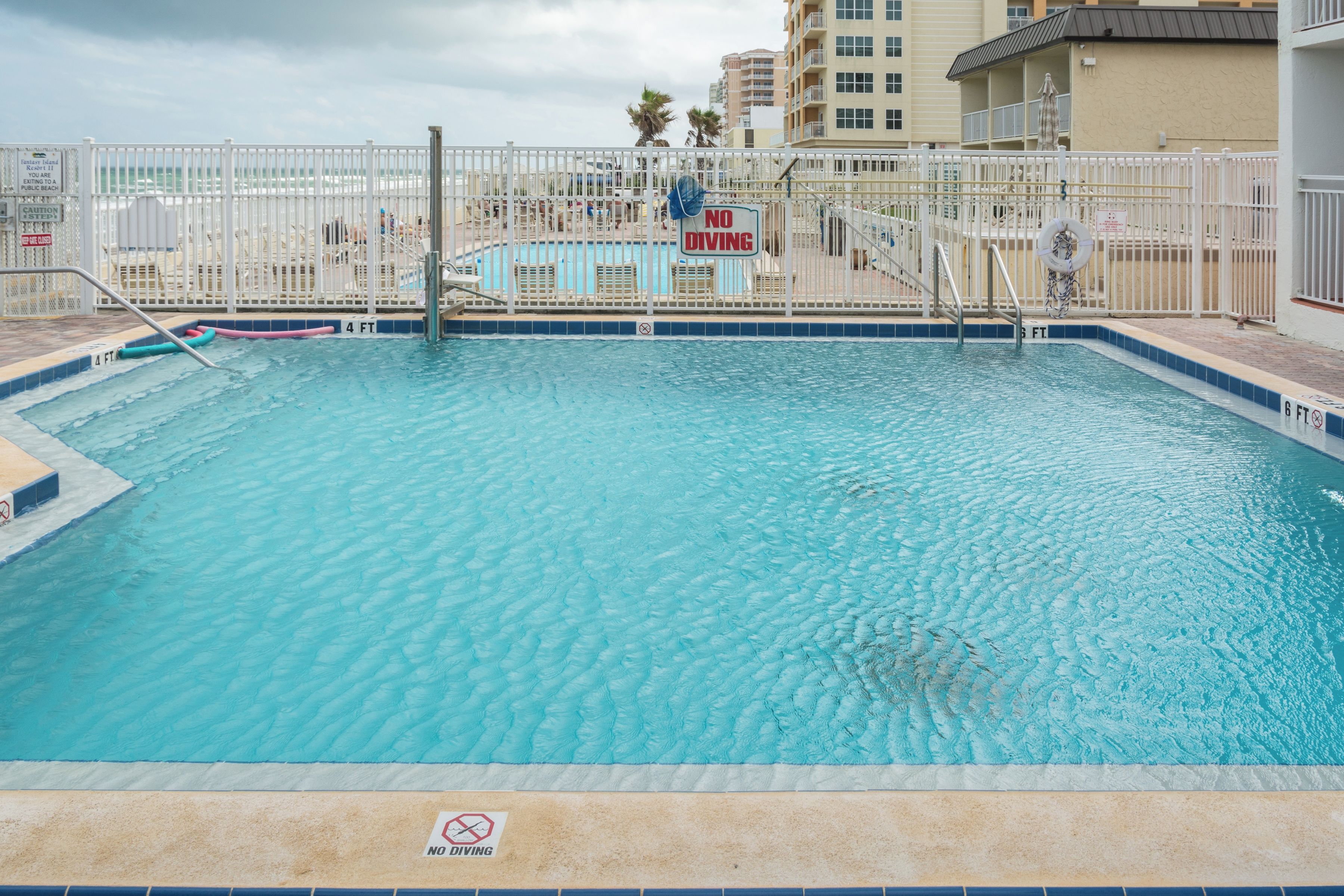 A swimming pool with a 'No Diving' sign, surrounded by a white fence, and a lifeguard tower in the background.
