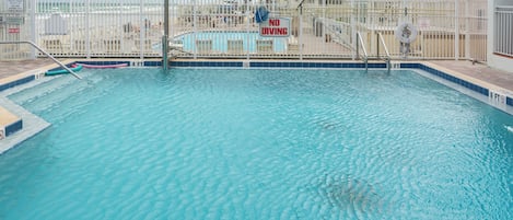 A swimming pool with a 'No Diving' sign, surrounded by a white fence, and a lifeguard tower in the background.