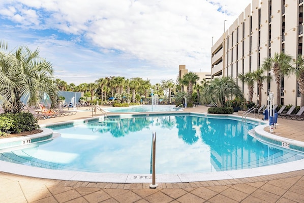 Une piscine dont la profondeur est indiquée à 3 pieds, entourée de palmiers et de chaises longues, avec un bâtiment visible à l’arrière-plan.