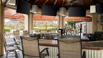 An outdoor bar area with seating, a bar counter, and multiple televisions.