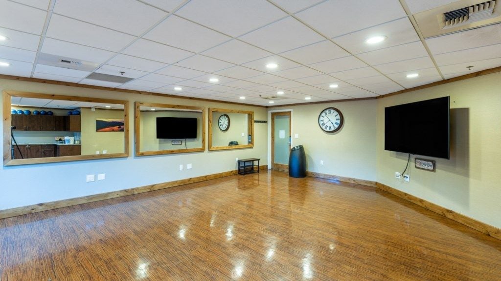 Une pièce spacieuse avec un plancher en bois, un grand miroir, une horloge et un téléviseur.