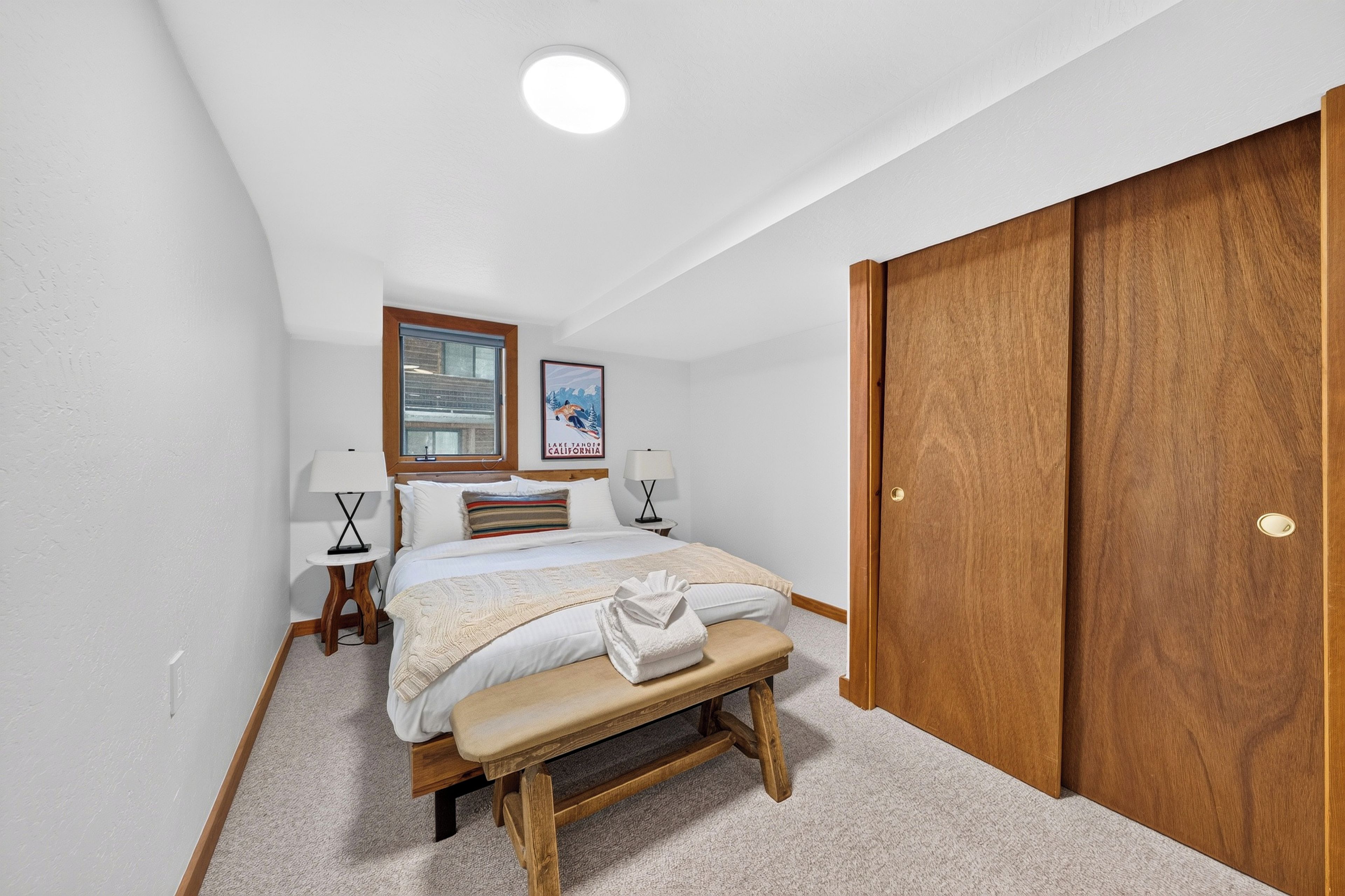 Une chambre à coucher avec un lit, des tables de chevet, un banc, une armoire et une affiche accrochée au mur.