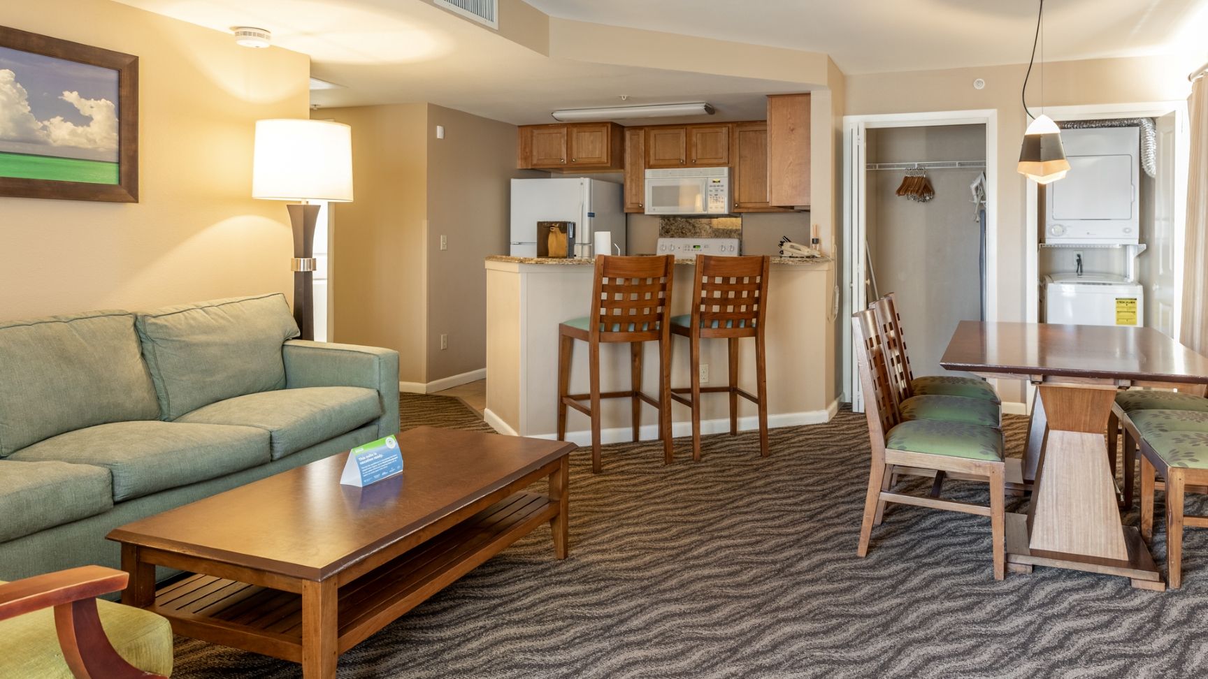 A living room with a sofa, coffee table, and chairs, a kitchen with wooden cabinets and appliances, and a dining area with a table and chairs.