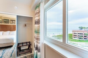 Habitación de hotel con cama, un pequeño rincón de descanso, una ventana y vistas a la playa y un edificio.