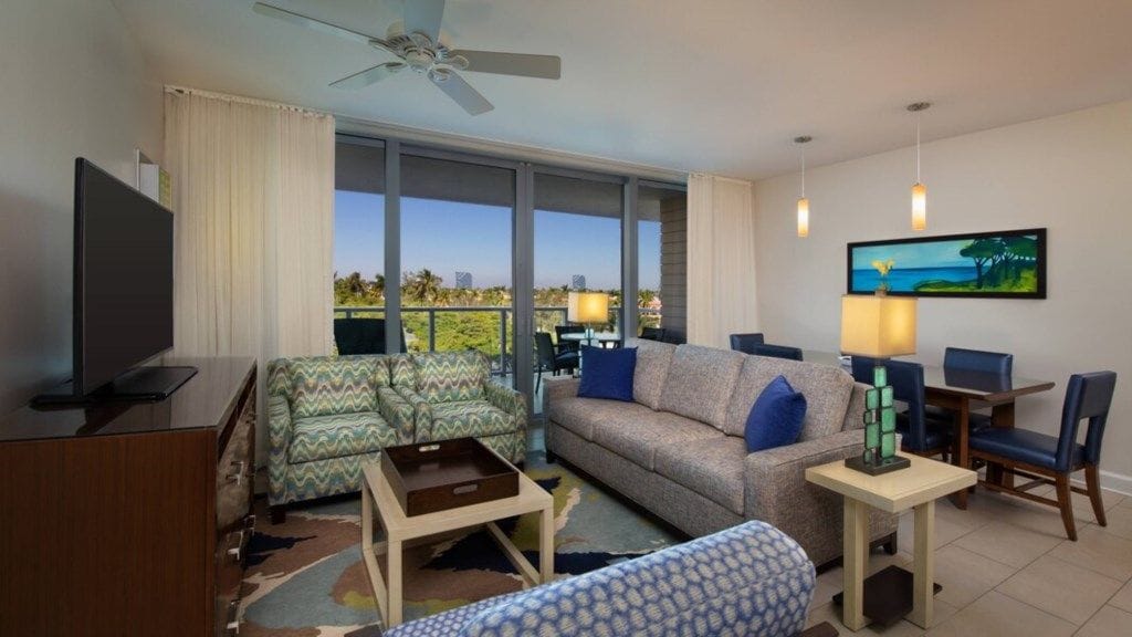 Una sala de estar moderna con un sofá, un sillón y un televisor. Hay un balcón con vistas al océano.