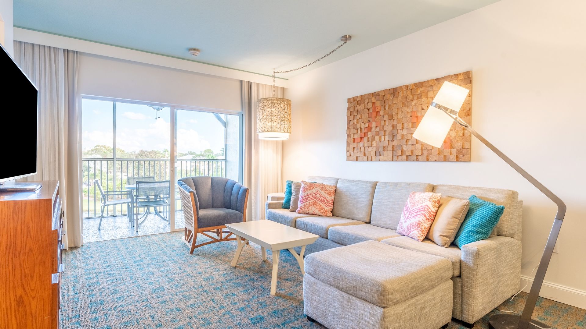 Un salon moderne avec un canapé, un fauteuil et une table basse. Il y a un balcon avec du mobilier d’extérieur et une grande fenêtre.
