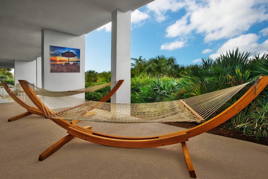 Silla hamaca con estructura de madera y asiento tejido, ubicada al aire libre con vista a follaje y un atardecer de fondo.