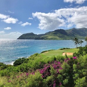 A coastal landscape with a golf course, lush greenery, and a clear view of the ocean and distant mountains. - Lihue | Family Island Retreat | Pool + Golf | 2BR Condo (Lihue)