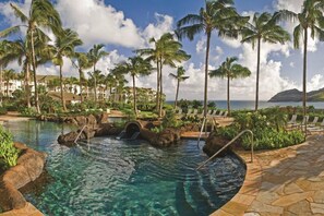 A resort pool with palm trees, lounge chairs, and a view of the ocean. - Lihue | Family Island Retreat | Pool + Golf | 2BR Condo (Lihue)