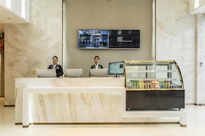Una recepción de hotel con dos empleados, un panel de exhibición digital y un mostrador de bebidas.